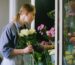A florist in an apron selects fresh white roses for a bouquet in a flower shop.